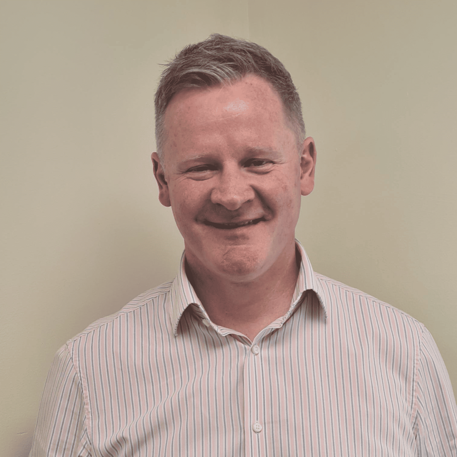 A man in a striped shirt smiling in front of a wall.